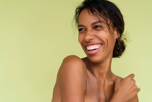 Beauty portrait of young topless african american woman with bare shoulders on green background with perfect skin and natural makeup - Photo, Image