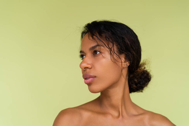 Πορτραίτο ομορφιάς νεαρής τόπλας αφροαμερικάνας γυναίκας με γυμνούς ώμους σε πράσινο φόντο με τέλειο δέρμα και φυσικό μακιγιάζ - Φωτογραφία, εικόνα