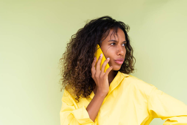 Bella donna africana americana in camicia casual su sfondo verde parlare sul telefono cellulare scioccato confuso - Foto, immagini