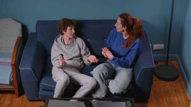 Gondoskodó anya beszél a fiával. Egy tinédzser otthon egy kék kanapén beszélget a szüleivel. Felnevelni egy gyereket egy anyától, komoly beszélgetés egy kamaszkorú tinivel. Kiváló minőségű 4k - Felvétel, videó