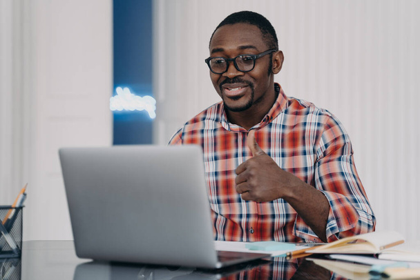African american young man showing thumb up gesture looking at laptop. Black guy student wearing glasses shows like sign, talking with friend by video call online, gives positive feedback. - Fotografie, Obrázek