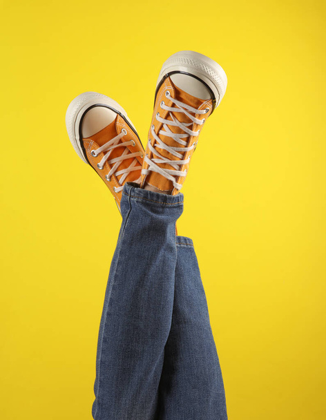 Female legs in jeans and stylish retro 80s yellow sneakers on a yellow background - Foto, imagen