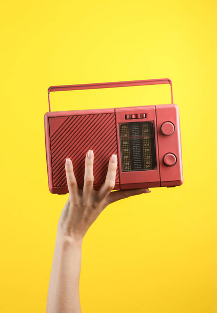 Жіноча рука тримає рожевий ретро-радіоприймач на жовтому тлі
 - Фото, зображення