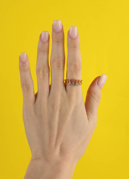 Golden ring in the form of crown with diamonds on female finger. Yellow background - Фото, изображение