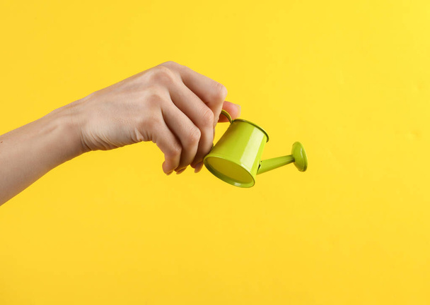Female hand holding a mini watering can on a yellow background - Foto, Imagem