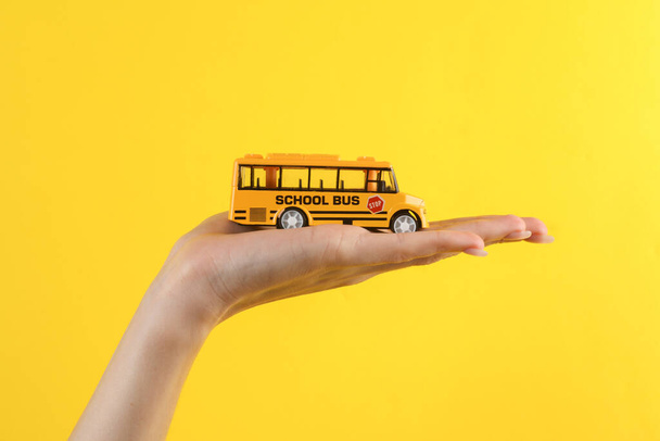 Woman's hand holding miniature of school bus on yellow background - Fotoğraf, Görsel