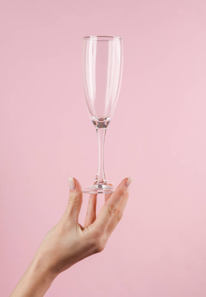 Пустой бокал шампанского в женской руке на розовом фоне - Фото, изображение