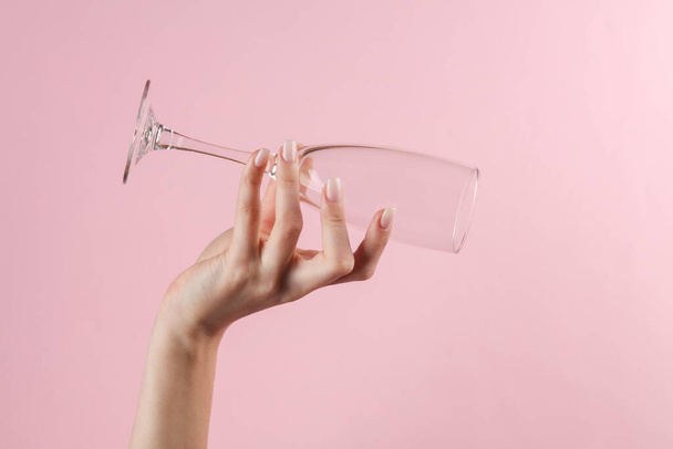 Empty champagne glass in a female hand on a pink background - Foto, imagen