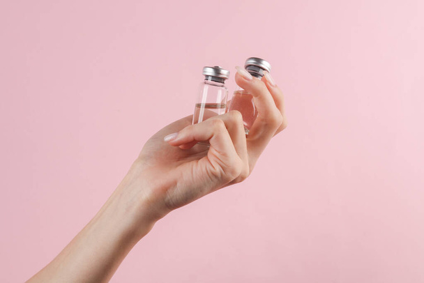 Impfflaschen in weiblicher Hand auf rosa Hintergrund - Foto, Bild