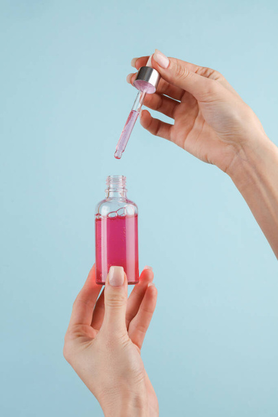 Serum bottle with a pipette in female hands on blue background - Fotó, kép