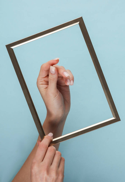 Main de femme à travers le cadre sur un fond bleu - Photo, image