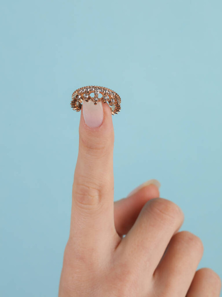 Bague en or en forme de couronne avec des diamants sur le doigt féminin. Fond bleu - Photo, image