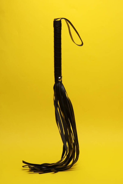 Leather sex whip levitating on yellow background. Dominance. Sex games. - Foto, Imagen
