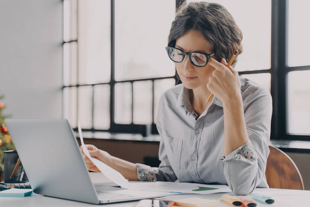 Jonge zakenvrouw met een bril die zich moe voelt, last heeft van oogspanning en vermoeidheid tijdens het computerwerk, overwerkte Spaanse vrouwelijke werknemer die de hele dag voor de laptop werkt - Foto, afbeelding