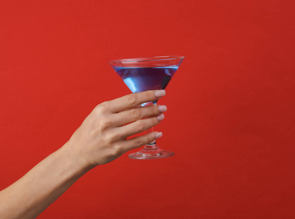 Женская рука с бокалом синего коктейля лагуны на красном фоне - Фото, изображение