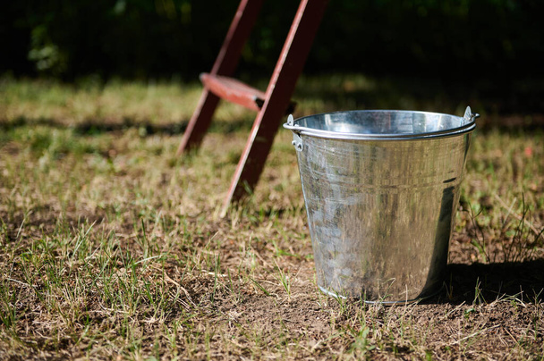 Still life with a metal galvanized bucket on the grass near the old stairs in the garden in the countryside. Harvest time. Gardening. Agriculture. Eco farming - Photo, Image