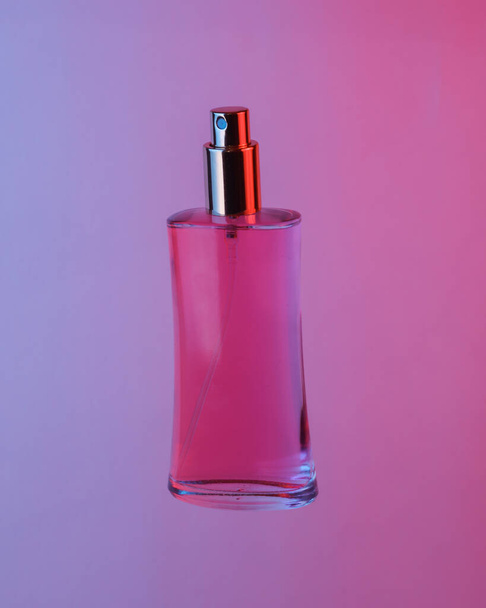 Pink perfume bottle floating in the air, isolated in blue-red neon gradient light. Levitating objects. Minimal fashion concept - 写真・画像