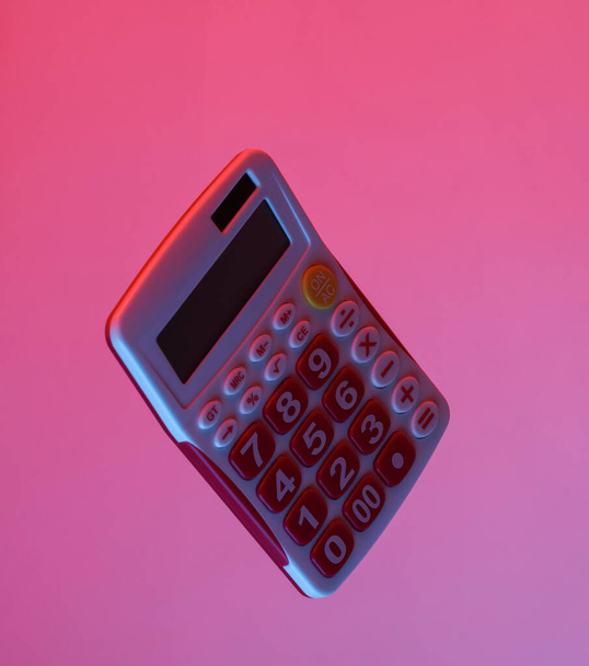 Calculator drijvend in de lucht, geïsoleerd in blauw-rood neon gradiënt licht. Zwevende objecten. Minimaal concept - Foto, afbeelding