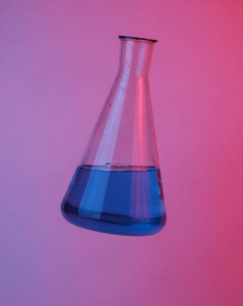 Laboratoriumkolf drijvend in de lucht, geïsoleerd in blauw-rood neon gradiënt licht. Zwevende objecten. Minimaal concept - Foto, afbeelding