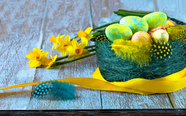 Pesä pääsiäismunia ja höyheniä, keltaisia daffodil kukkia ja keltainen nauha, lähikuva. Hyvää pääsiäistä käsite. - Valokuva, kuva