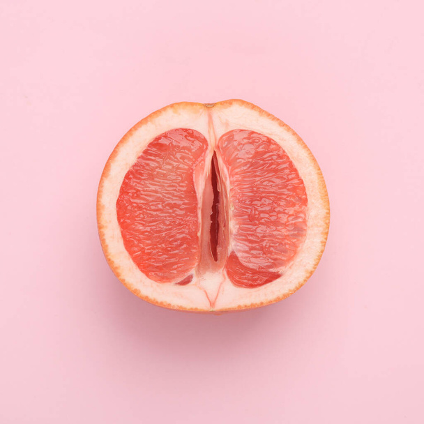 Gynecology, female intimate hygiene. Half of a ripe grapefruit symbolizing the female vagina on a pink background. Creative idea, allegory, fresh idea. Top view - Foto, afbeelding