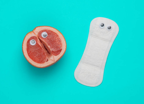 Gynecology, female intimate hygiene, menstruation. Half of grapefruit symbolizing female vagina and pads with eyes on blue background. Top view - Φωτογραφία, εικόνα