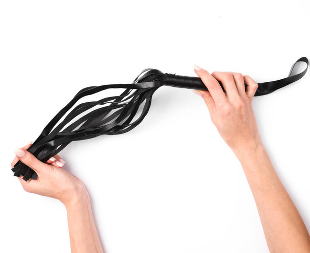 Female hands hold a leather whip from sex shop on a white background - Φωτογραφία, εικόνα