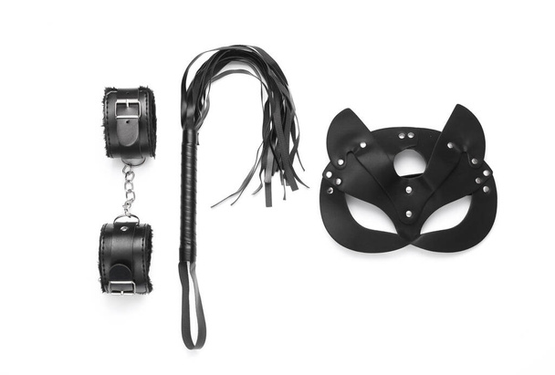 Кожаные наручники и кнут с маской из секс-шопа на белом фоне. Вид сверху. Плоский лежал - Фото, изображение