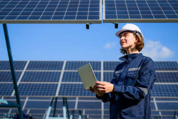 Female engineer holding laptop checking solar panels at industrial solar cell farm, Engineer working at power station, Electric system maintenance at solar panels field, Eco friendly and clean energy - Fotoğraf, Görsel