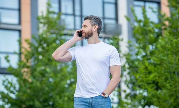adult man has phone call outdoor. man having phone call in the street. man call on phone outside. photo of man call on phone and talk. - Photo, Image