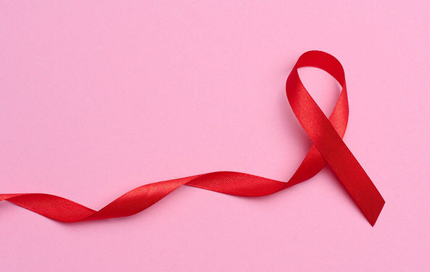 Pembe arka planda bir fiyonk şeklinde ipek kırmızı kurdele, AIDS 'le mücadelenin sembolü ve dayanışma ve destek işareti. - Fotoğraf, Görsel