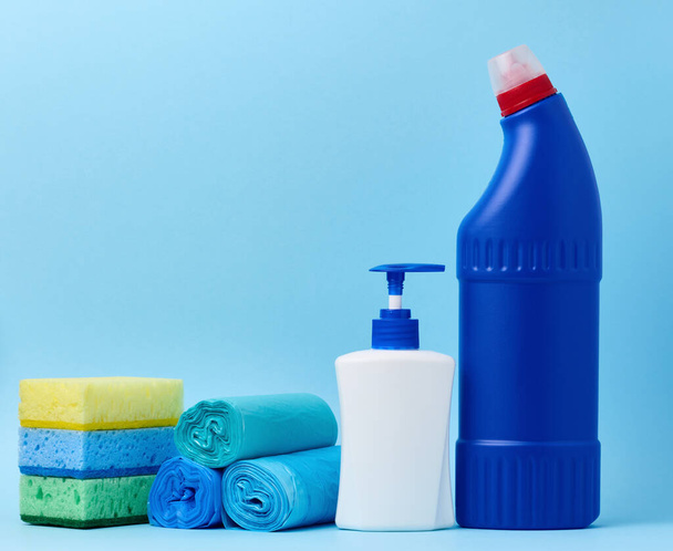 Weiße Plastikflasche mit Spender und Müllsäcken, Schwämmen und einer blauen Flasche mit Waschmittel auf blauem Hintergrund - Foto, Bild