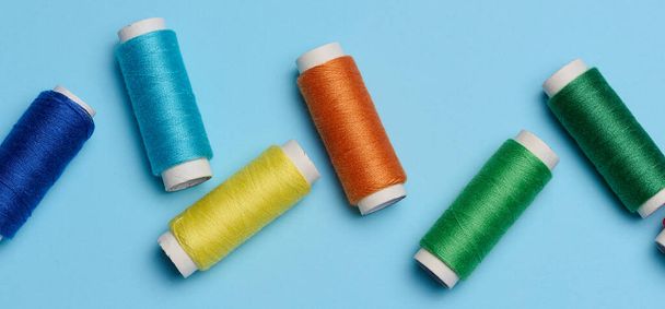 Bobinas multicolores de hilos de coser sobre un fondo azul, vista superior - Foto, imagen