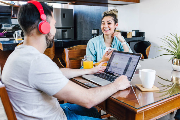 young latin couple working on laptop with headphones at home in Mexico, hispanic people home office - Foto, afbeelding