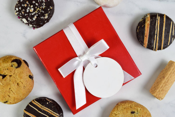 Closeup of red present with blank white tag surrounded by tempting cookies. - Foto, afbeelding
