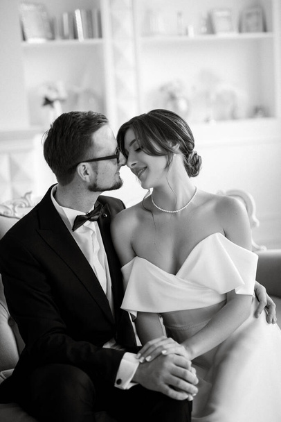 groom in a black suit with a bow tie and the bride in a tight white dress in a bright studio - Photo, Image