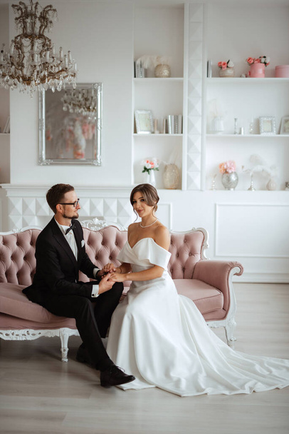 groom in a black suit with a bow tie and the bride in a tight white dress in a bright studio - Foto, Imagen