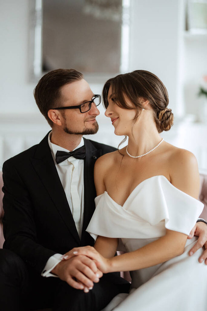 groom in a black suit with a bow tie and the bride in a tight white dress in a bright studio - Fotó, kép