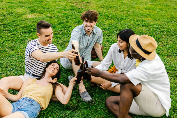 Ευτυχισμένοι νέοι χιλιετίες ομάδα των διαφόρων φίλων επευφημίες με μπύρες Google και κοινωνική συγκέντρωση μαζί στο πάρκο της πόλης. Σχέδιο συνάντησης και επανένωσης - Φωτογραφία, εικόνα