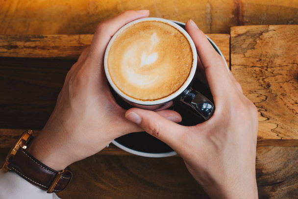 Iemand die een hete kop cappuccino koffie in zijn of haar handen houdt. Een cappuccino is de perfecte balans tussen espresso, gestoomde melk en schuim. - Foto, afbeelding