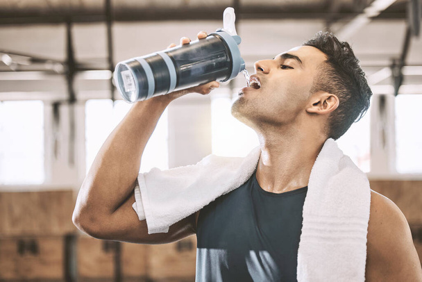 Young athlete drinking water after a workout. Fit man taking a break to hydrate. Always have a water bottle when exercising at the gym. Bodybuilder drinking from a water bottle in the gym. - Фото, изображение