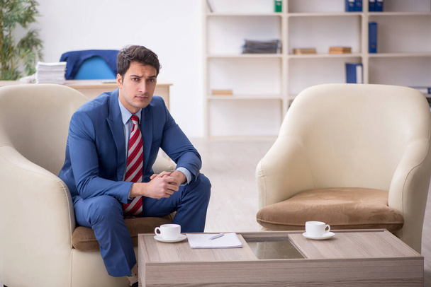 Νεαρός επιχειρηματίας υπάλληλος που κάθεται στο χώρο εργασίας - Φωτογραφία, εικόνα
