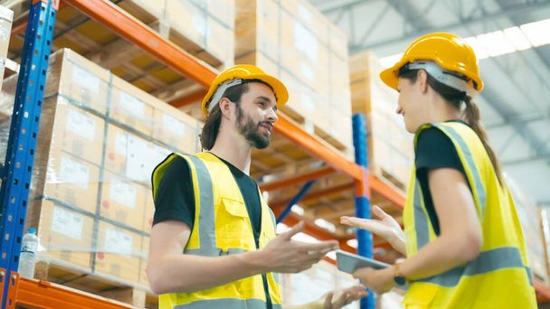 Smiling workers in distribution warehouse having a cheerful conversation. They wearing vest and safety helmet in work - Photo, Image