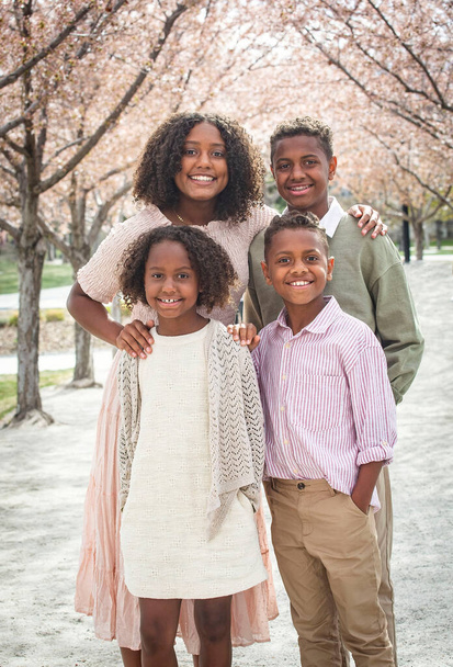 Portret pięknej grupy różnorodnych dzieci stojących w rzędzie drzew wiśniowych. Uśmiechnięte afro-amerykańskie rodzeństwo pozujące razem. Zróżnicowana koncepcja rodziny - Zdjęcie, obraz