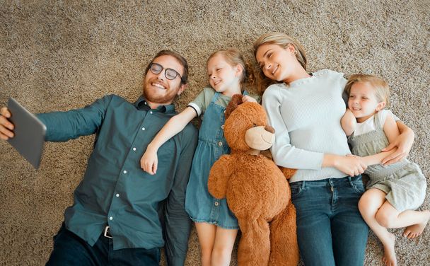 Lach naar de camera. Hoge hoek opname van een jong gezin liggend op de woonkamer vloer en met behulp van een digitale tablet - Foto, afbeelding