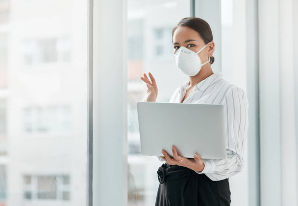 Сохранить мой бизнес во время кризиса вызов принят. молодая деловая женщина в маске, держащая ноутбук и машущая из окна в современном офисе - Фото, изображение