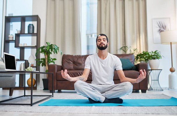 Medicatie is het geestesmedicijn. een knappe jongeman die thuis yoga beoefent in zijn woonkamer - Foto, afbeelding