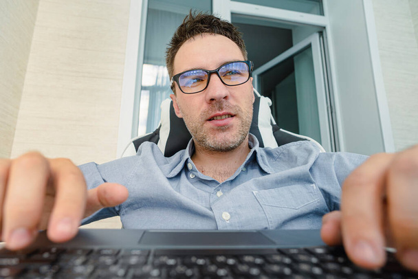 Un joven guapo con una camisa azul está trabajando en una computadora sobre un fondo claro. El programador se centra en el trabajo. - Foto, imagen