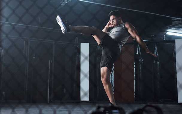 Hes a force to be reckoned with. a young man practicing his kickboxing routine at a gym - Foto, imagen