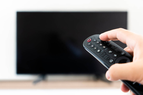The man with the remote control in hand watching the sports channel and presses the button on the remote control. Remote control in hand closeup. - Foto, Imagen